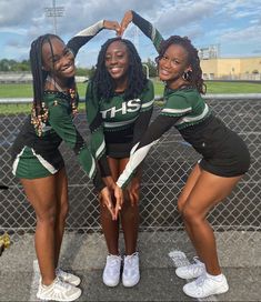 three cheerleaders posing for a photo in front of a fence