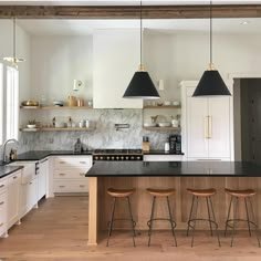 a large kitchen with white cabinets and black counter tops, two pendant lights hanging over the island