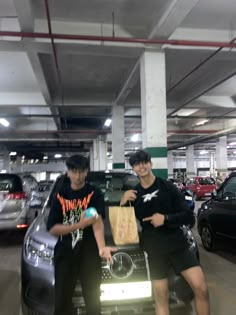 two young men standing next to each other in a parking garage with cars parked behind them