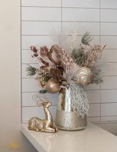 a silver vase filled with lots of flowers on top of a white counter next to a deer figurine