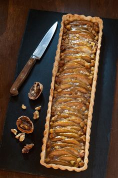 an apple tart sitting on top of a table next to a knife and some nuts