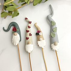 four decorated toothpicks sitting on top of a white table next to green leaves