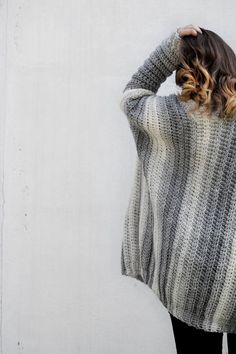 a woman standing in front of a white wall with her hands on her head wearing a sweater