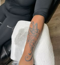 a woman sitting in a chair with a tattoo on her arm and leg behind her