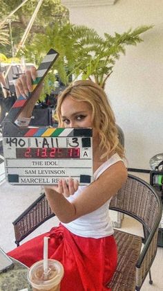 a woman sitting at a table holding up a stack of movie claps with a drink in front of her