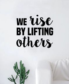 we rise by lifting others wall decal in black on a white wall next to a couch