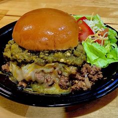 a black plate topped with a cheeseburger and lettuce