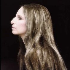 a woman with long hair standing in front of a black background and looking off to the side