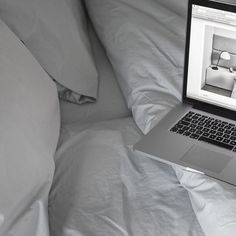 an open laptop computer sitting on top of a bed covered in white sheets and pillows