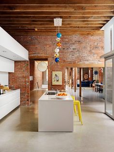 an open kitchen and dining room with exposed brick walls, white cabinets and yellow chairs