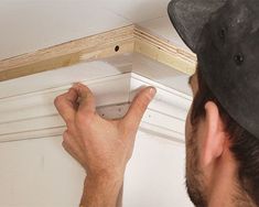 a man is working on the ceiling with screws in his hand and an unfinished piece of wood behind him