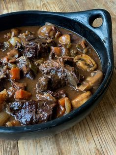 a bowl filled with beef stew and carrots on top of a wooden table next to a fork