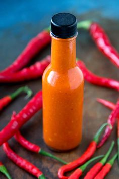 a bottle filled with hot sauce sitting on top of a table next to red chili peppers