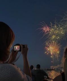 people watching fireworks on the water at night with their cell phones in front of them