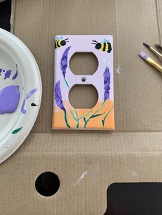 a painted light switch cover sitting on top of a cardboard box next to a white plate