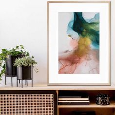 an abstract painting hangs on the wall next to a shelf with books and plant pots