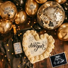 a heart shaped cake sitting on top of a wooden table next to gold balloons and disco balls