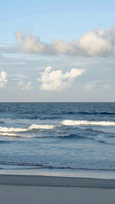 a person walking on the beach with a surfboard in hand and clouds in the background