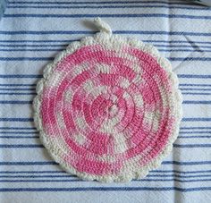 a pink and white crocheted dishcloth on a striped table cloth with scissors