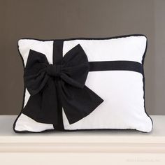 a black and white pillow with a large bow on it's side, sitting on a shelf