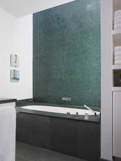 there is a bathtub and towels in the bathroom with green tiles on the wall