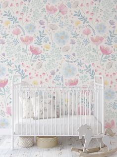 a white crib in front of a floral wallpaper with pink, blue and yellow flowers