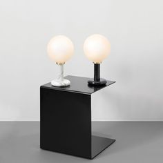 two lamps sitting on top of a black table next to each other in front of a white wall