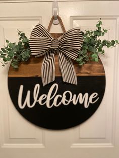 a welcome sign hanging on a door with a bow and greenery in the center