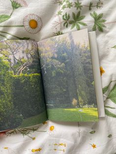 an open book sitting on top of a bed next to a flower covered comforter