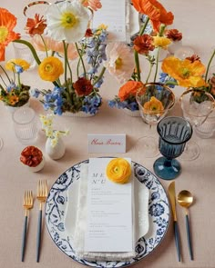 the table is set with blue and white plates, silverware, and colorful flowers