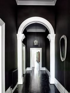 an empty hallway with black walls and white trim on the ceiling, along with arched doorways