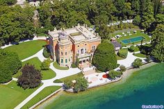 an aerial view of a large mansion in the middle of a lake with trees surrounding it