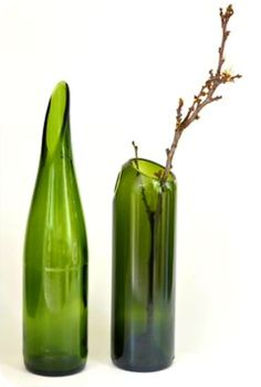 two green vases sitting next to each other on a white surface with a twig sticking out of one