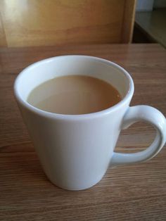 a white cup filled with liquid sitting on top of a wooden table next to a window