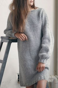 a woman standing next to a ladder wearing a gray sweater dress