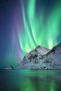 the northern lights shine brightly over snow covered mountains and water in this photo from norway