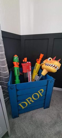 a toy box filled with different types of toys on the floor next to a wall