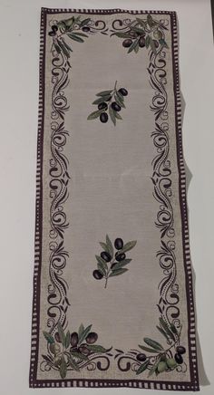 an embroidered table runner with olives and vines on the border, hanging from a wall