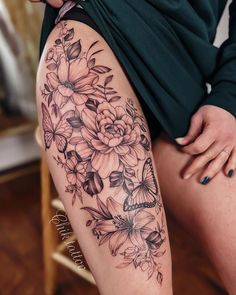 a woman's thigh with flowers and butterflies tattoo on her leg, while she is sitting in a chair