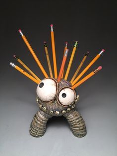 a sculpture with many pencils sticking out of it's face and eyes, in front of a gray background