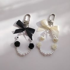 two key chains with bows and pearls attached to them on a white surface, one is black and the other is white