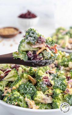 broccoli and cranberry salad being lifted from a white bowl with a wooden spoon