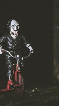 a creepy clown riding a red bike in the dark with his face painted on it