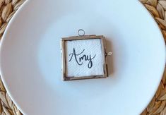 a white plate topped with a small square frame on top of a wooden table next to a woven place mat