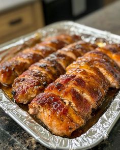 meat wrapped in tinfoil sitting on top of a metal pan filled with sauces