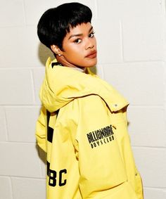 a young person wearing a yellow jacket with the number 8 on it, standing in front of a white brick wall