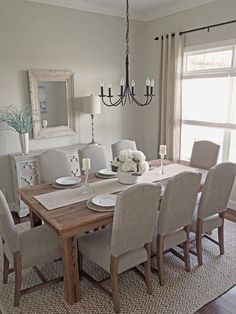 the dining room table is set with white plates and place settings on it, along with gray upholstered chairs