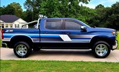 a blue pickup truck parked on the side of a driveway in front of a house