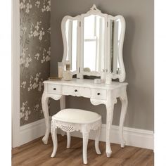 a white dressing table with mirror and stool next to a wallpapered hallway area