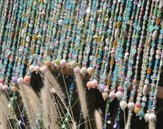 beads hanging from the side of a building with grass and flowers in front of it